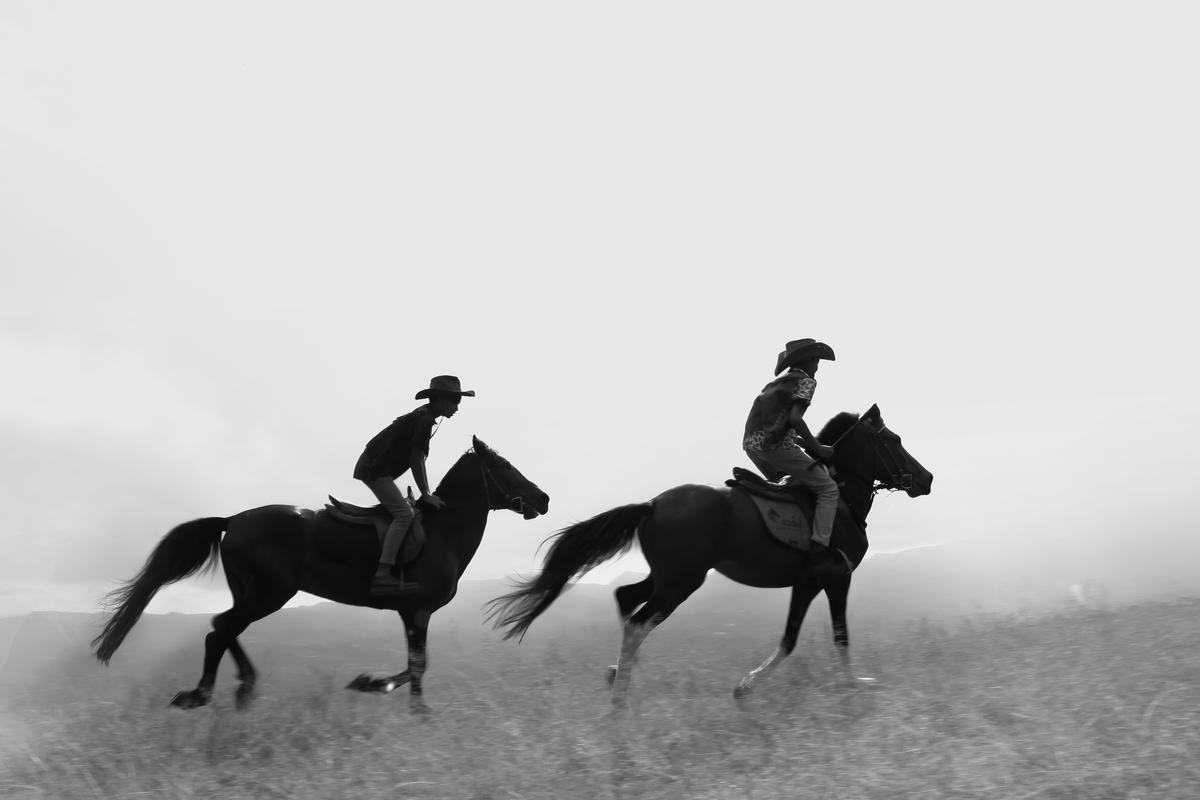 Black and white photo of two young riders racing horses across an open field