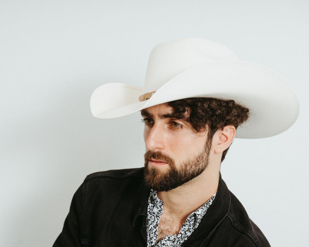 Studio portrait of a bearded man wearing a white cowboy hat and black denim jacket